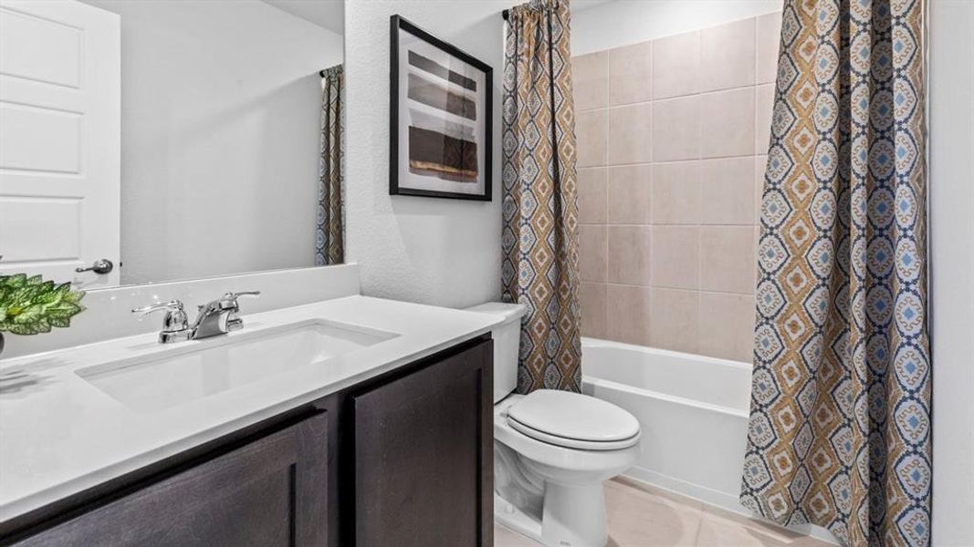 Bathroom featuring a white integrated sink with chrome faucet, dark wood-finish vanity cabinetry, a built-in bathtub with a tiled surround, and a wall-mounted toilet Bathroom featuring a white integrated sink with chrome faucet, dark wood-finish vanity cabinetry, a built-in bathtub with a tiled surround, and a wall-mounted toilet