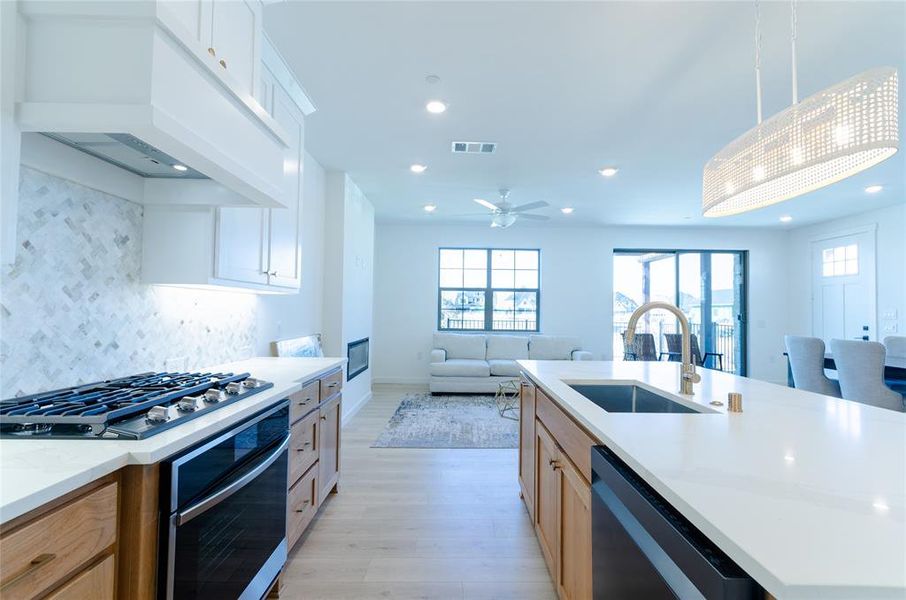 Kitchen featuring stainless steel appliances, light stone countertops, open floor plan, light wood-type flooring, and backsplash