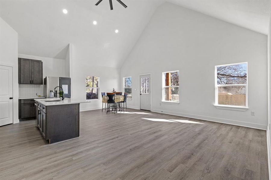 Kitchen with light hardwood / wood-style flooring, high vaulted ceiling, tasteful backsplash, and an island with sink