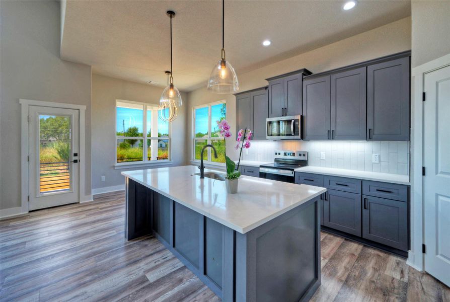 Modern cabinetry and a central island ground this open kitchen with warm wood-look flooring. Modern cabinetry and a central island ground this open kitchen with warm wood-look flooring.