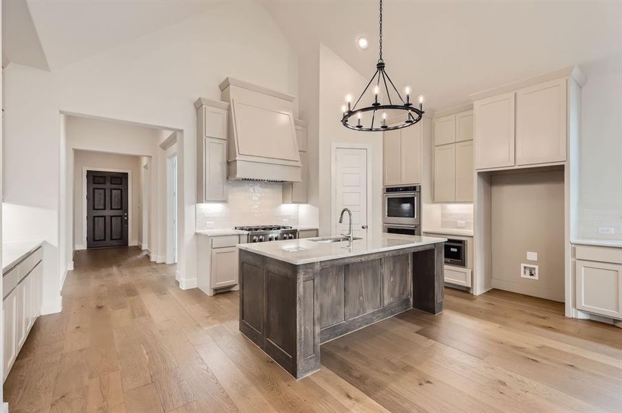 Kitchen with light hardwood / wood-style floors, sink, an island with sink, high vaulted ceiling, and stainless steel appliances