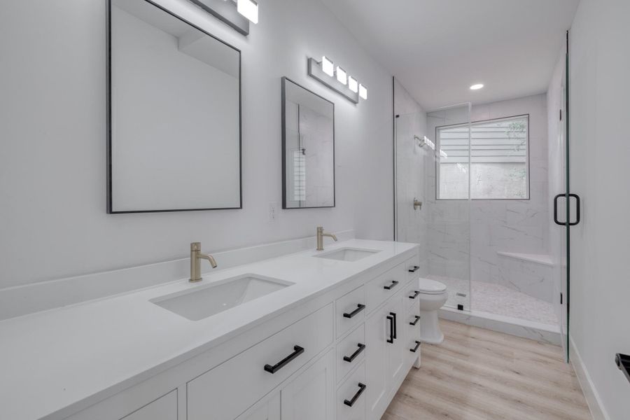 A well-lit primary bathroom features a dual vanity, a glass-enclosed shower, and sleek modern fixtures. A well-lit primary bathroom features a dual vanity, a glass-enclosed shower, and sleek modern fixtures.