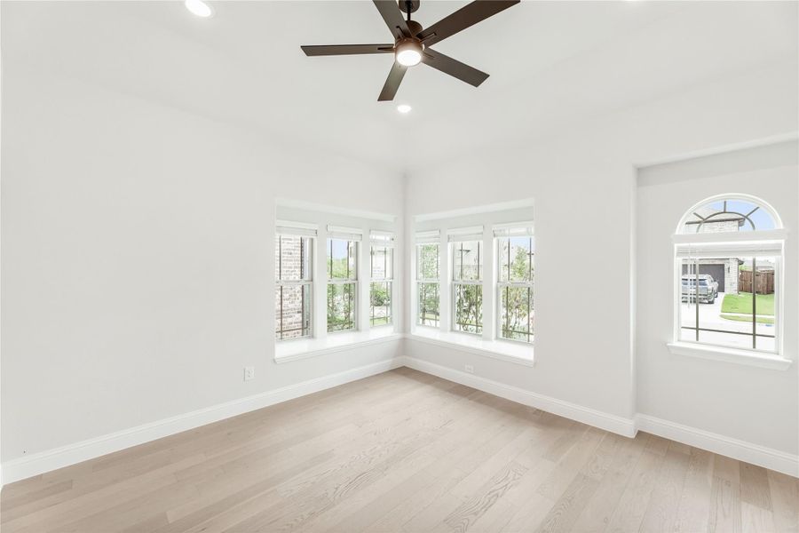 Empty room with light wood floors, ceiling fan, corner windows, and an arched window