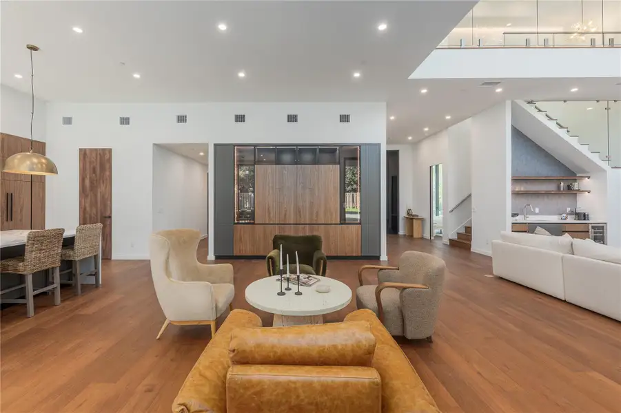 Rich hardwood floors unite an open concept living space, featuring a built-in bar and seamless flow to the kitchen.