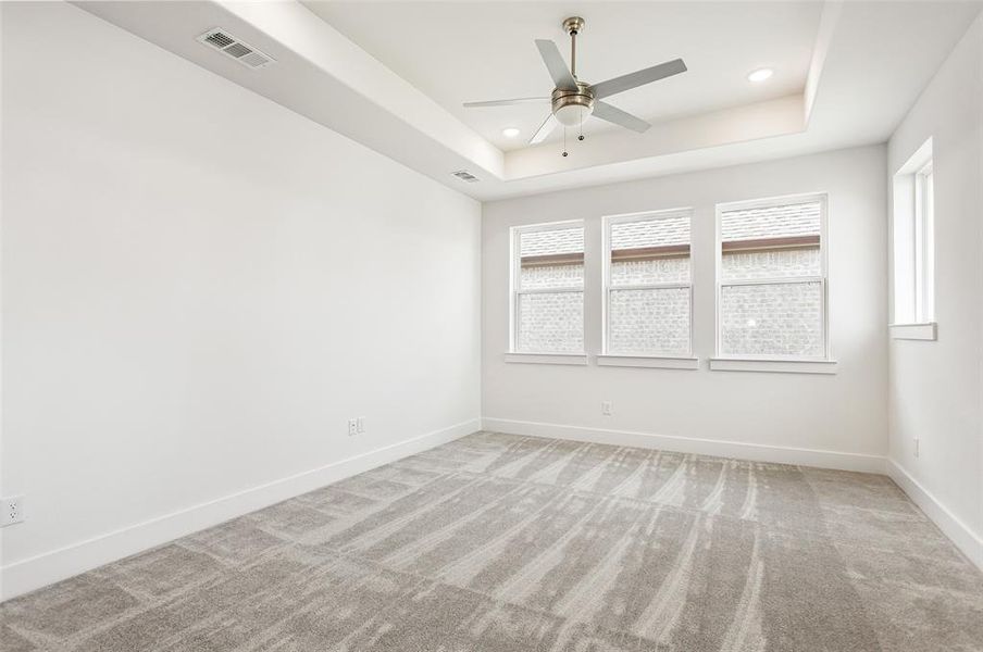 Carpeted spare room featuring ceiling fan and a tray ceiling