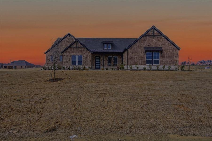 View of front of property with a standing seam roof, brick siding, and a front lawn