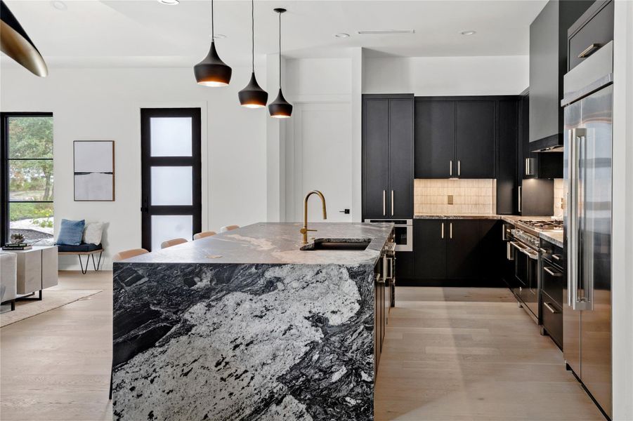 Kitchen featuring light stone counters, backsplash, dark cabinetry, hanging light fixtures, and premium appliances