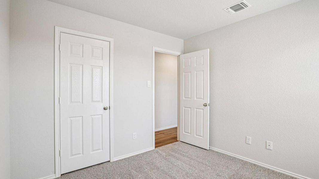 Carpeted room featuring light gray walls, white baseboards, and two paneled interior doors Carpeted room featuring light gray walls, white baseboards, and two paneled interior doors