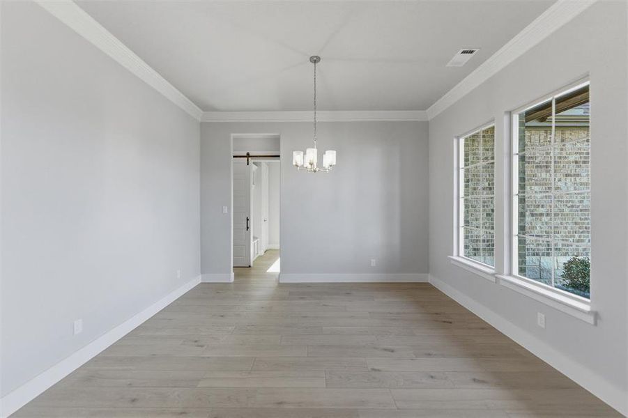 Unfurnished dining area with crown molding, light wood-style flooring, suspended lighting, and a barn door