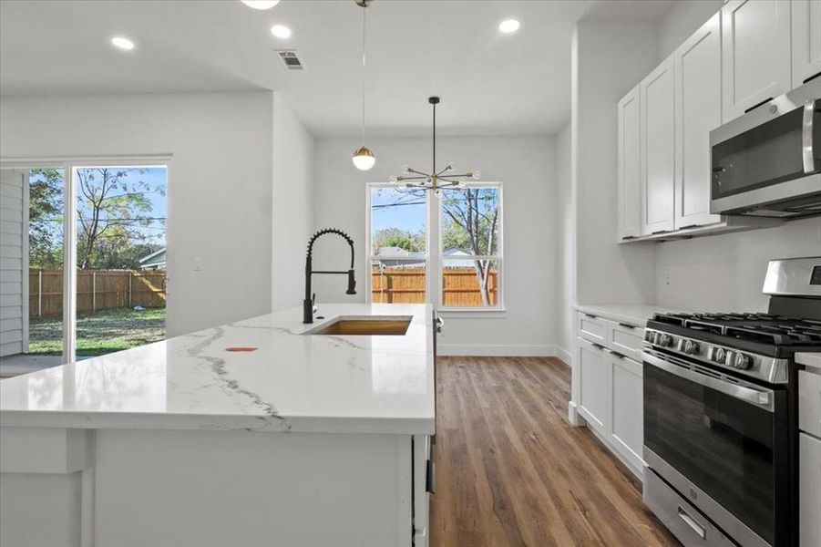 Kitchen with stainless steel appliances, white cabinets, recessed lighting, light wood-type flooring, and decorative light fixtures