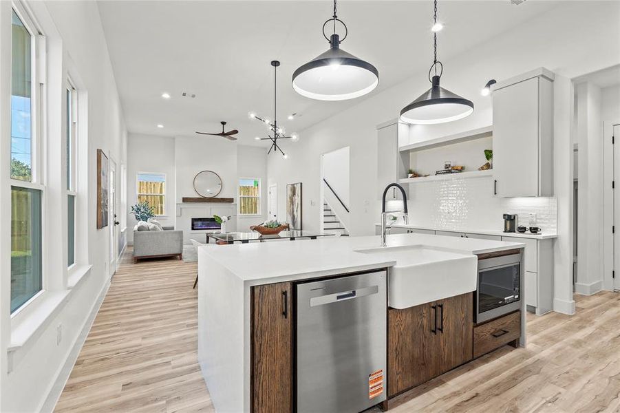 Kitchen featuring appliances with stainless steel finishes, decorative light fixtures, an island with sink, tasteful backsplash, and open floor plan
