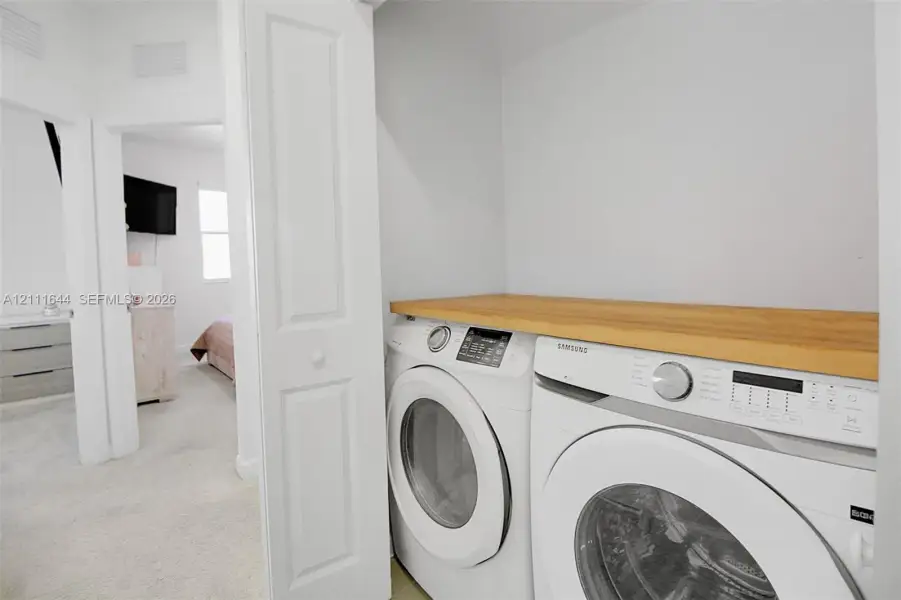 Laundry closet featuring stacked front-loading appliances and a built-in wood-finish folding counter Laundry closet featuring stacked front-loading appliances and a built-in wood-finish folding counter