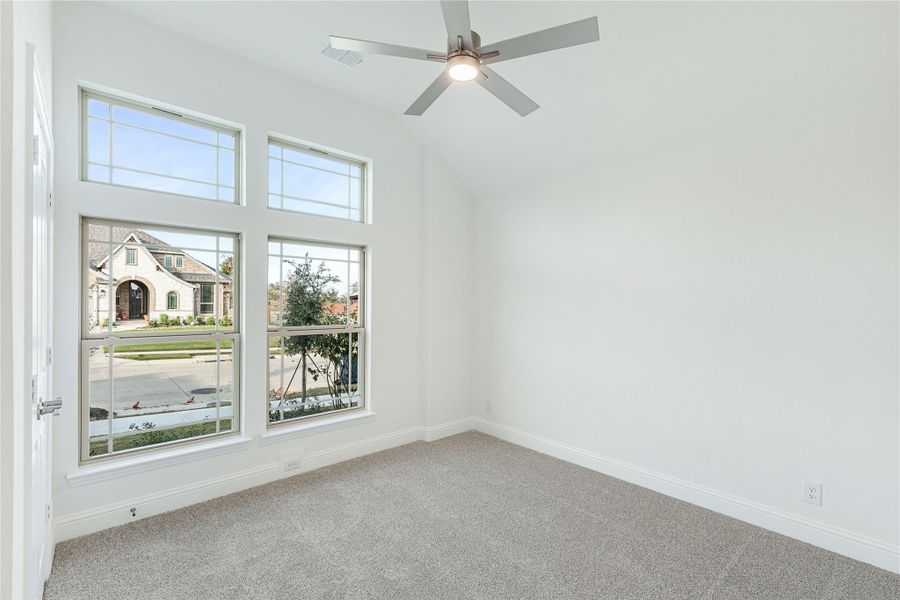 Empty bedroom with gray carpet, ceiling fan, and large windows overlooking a neighborhood street