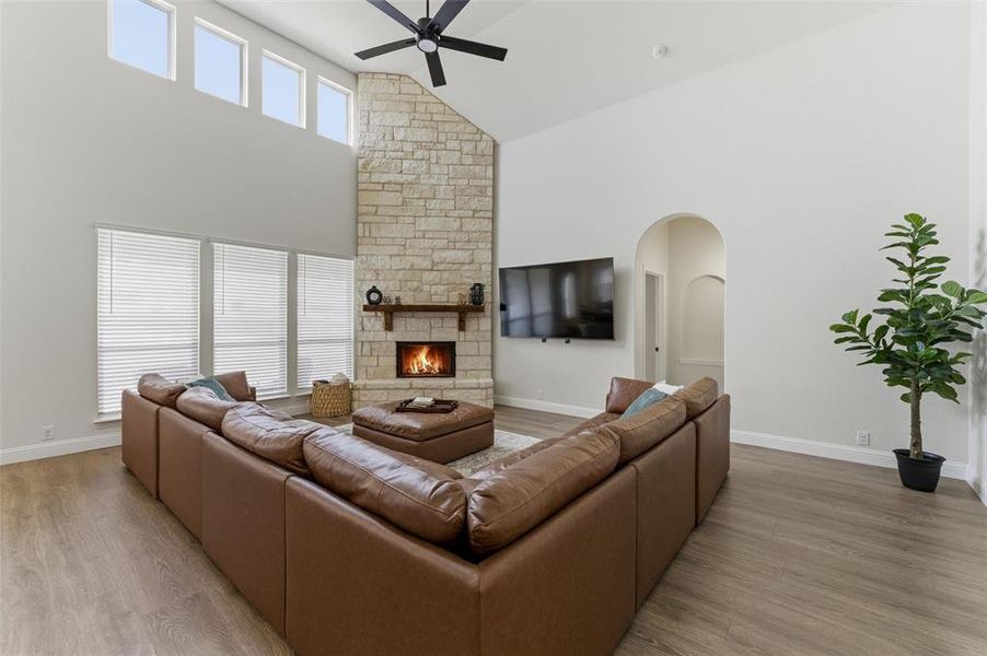 Living room featuring arched walkways, a stone fireplace, ceiling fan, vaulted ceiling, and light wood-style flooring