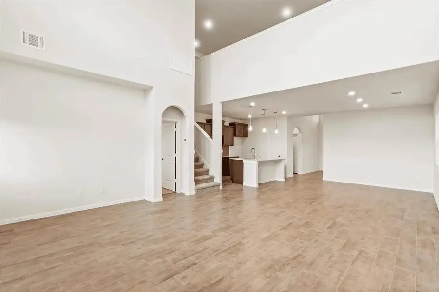 Expansive open-concept living area with soaring ceilings and rich wood-look tile flooring. The space flows effortlessly from the family room into the kitchen and dining areas, creating an ideal setting for daily living and entertaining. Recessed lighting and large windows flood the space with natural light, highlighting the home’s generous proportions and clean architectural lines.