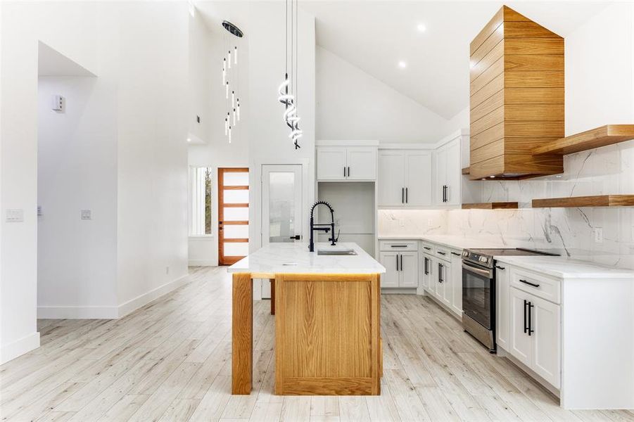 Kitchen with high vaulted ceiling, tasteful backsplash, white cabinets, light wood finished floors, and electric stove Kitchen with high vaulted ceiling, tasteful backsplash, white cabinets, light wood finished floors, and electric stove
