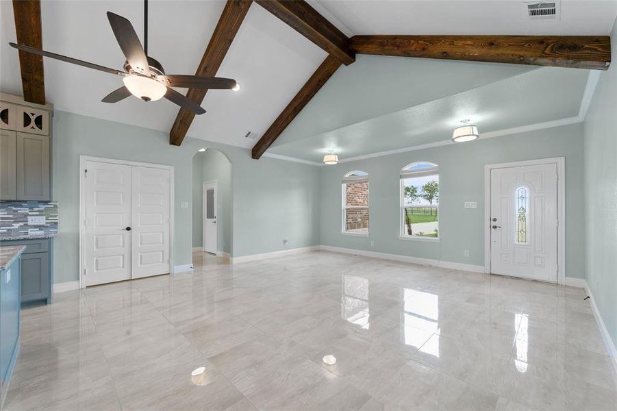 Unfurnished living room with crown molding, lofted ceiling with beams, light tile patterned floors, and ceiling fan