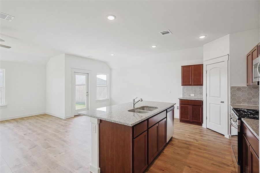 Kitchen featuring sink, light stone counters, light hardwood / wood-style flooring, a center island with sink, and appliances with stainless steel finishes