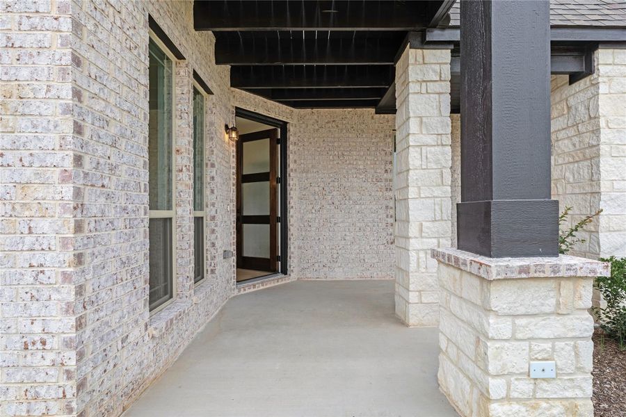 Covered front porch with brick and stone exterior, dark wood columns, and glass-panel entry door Covered front porch with brick and stone exterior, dark wood columns, and glass-panel entry door