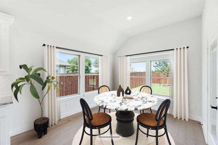 Bright dining area with round marble table, four chairs, vaulted ceiling, and large windows overlooking backyard