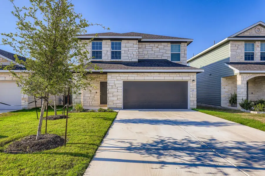 View of front of property featuring stone siding, driveway, a shingled roof, an attached garage, and a front yard