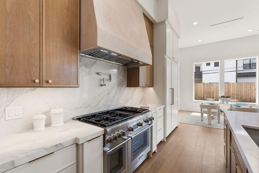 A professional-grade range is framed by a custom plaster vent hood, flanked by white oak cabinetry and a full-height quartzite backsplash, blending performance with refined design.