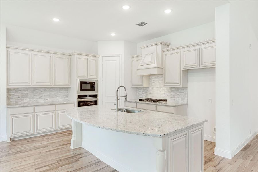 White kitchen with granite island, raised-panel cabinets, stone backsplash, and light hardwood floors