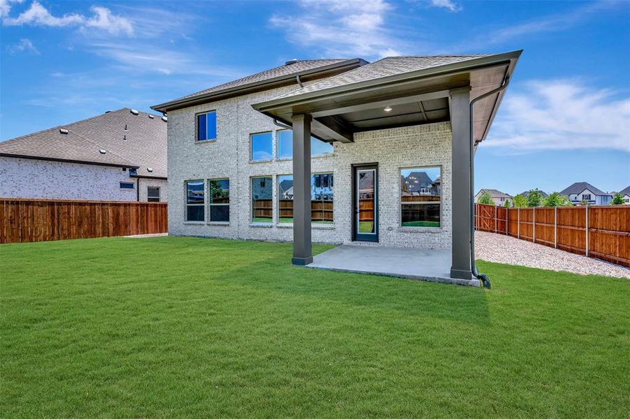 Spacious backyard featuring a covered patio, extensive lawn, gray brick exterior, multiple large windows, and a wood privacy fence