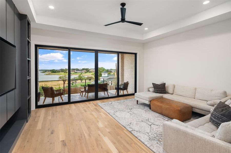 Expansive game room designed to maximize the breathtaking lake views, featuring a dramatic wall of sliding glass doors that open to a private balcony overlooking the water. Hardwood floors, a tray ceiling with accent lighting, and built-in speakers create the perfect space for relaxing or entertaining while enjoying the stunning scenery.