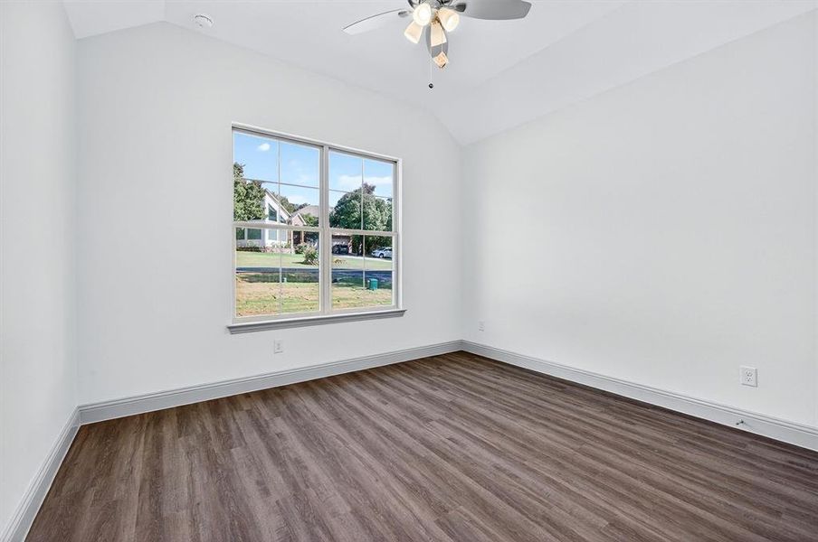 Spare room featuring wood finished floors, vaulted ceiling, and a ceiling fan