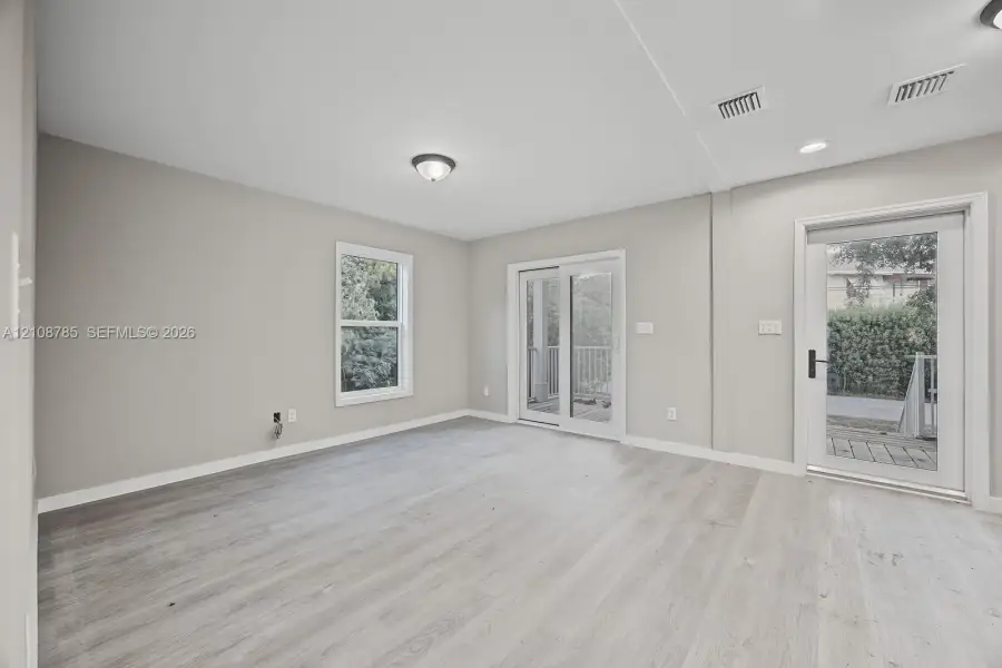 Neutral-toned interior space featuring wood-finish flooring, sliding glass patio doors, a separate exterior door with a glass pane, and recessed ceiling lighting Neutral-toned interior space featuring wood-finish flooring, sliding glass patio doors, a separate exterior door with a glass pane, and recessed ceiling lighting