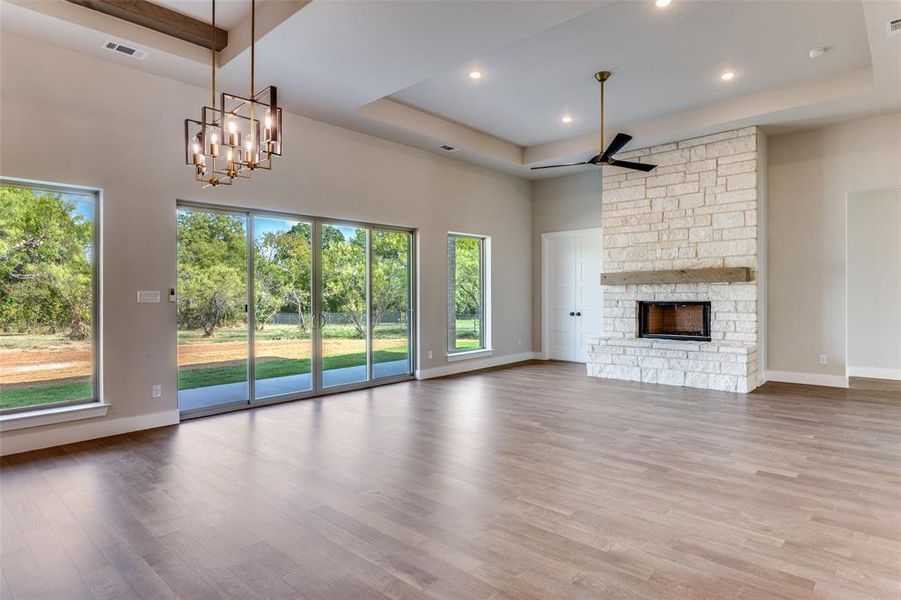 Unfurnished living room with a tray ceiling, light wood-style floors, a fireplace, a ceiling fan, and recessed lighting Unfurnished living room with a tray ceiling, light wood-style floors, a fireplace, a ceiling fan, and recessed lighting