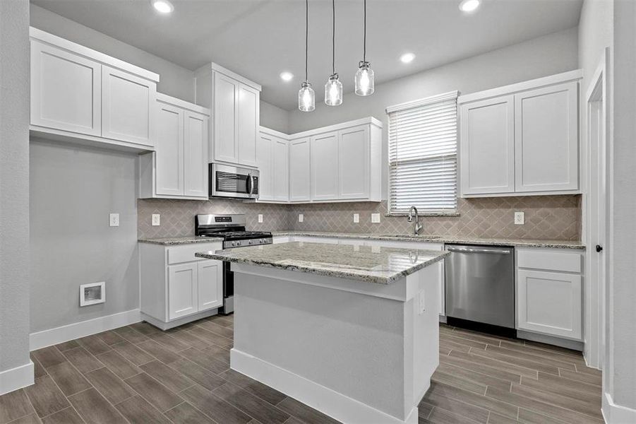 Kitchen featuring white cabinetry, appliances with stainless steel finishes, light stone countertops, a center island, and pendant lighting