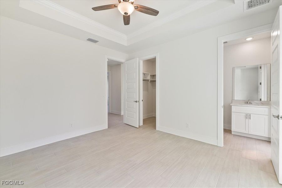 Unfurnished bedroom with a tray ceiling, a walk in closet, ensuite bathroom, ceiling fan, and crown molding