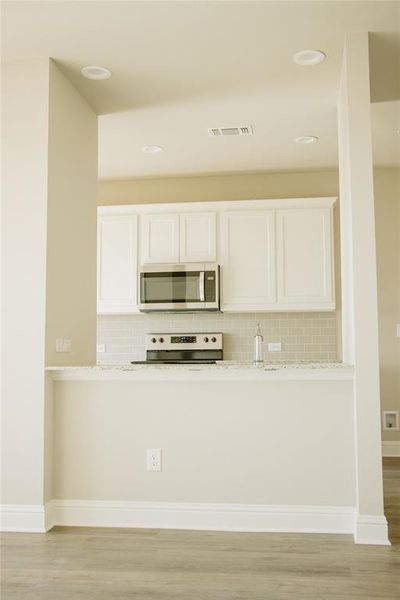 Kitchen with tasteful backsplash, light stone counters, light hardwood / wood-style flooring, stove, and white cabinets