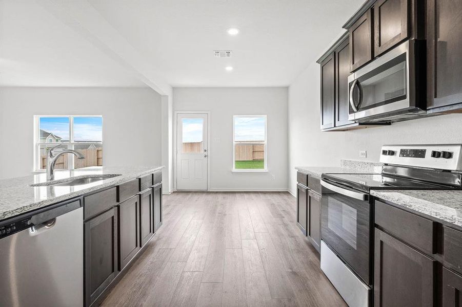 Kitchen featuring stainless steel appliances, light stone counters, sink, and light wood-type flooring