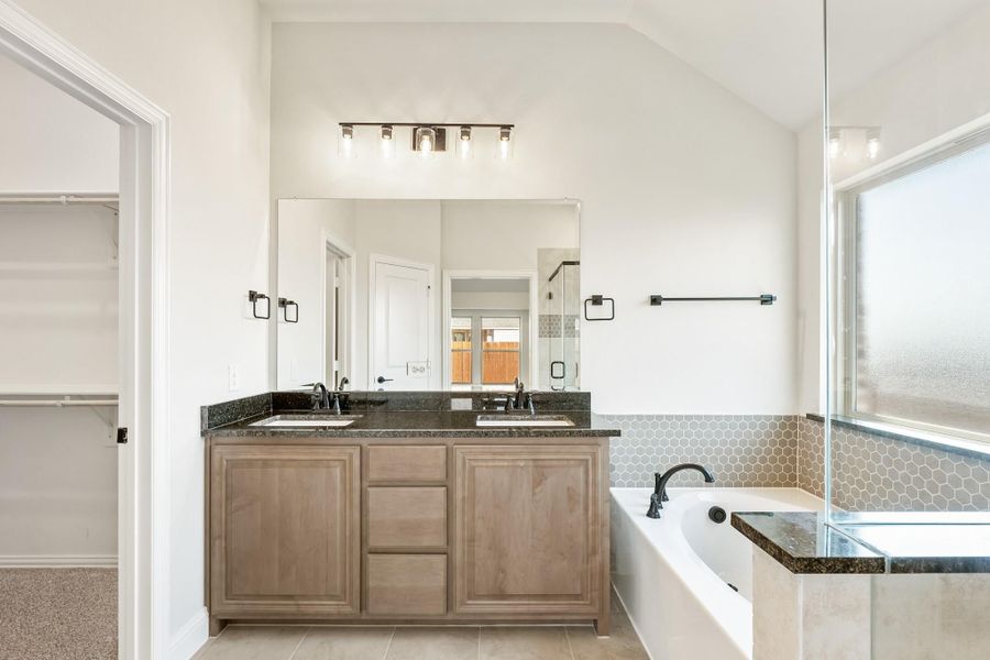 Master bathroom with double vanity, dark granite countertops, soaking tub, and vaulted ceiling Master bathroom with double vanity, dark granite countertops, soaking tub, and vaulted ceiling