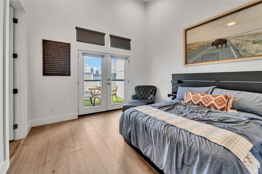 Bedroom featuring access to exterior, light wood finished floors, french doors, and a high ceiling Bedroom featuring access to exterior, light wood finished floors, french doors, and a high ceiling