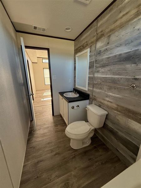 Half bath featuring vanity, dark wood-style floors, wood walls, a textured ceiling, and ornamental molding