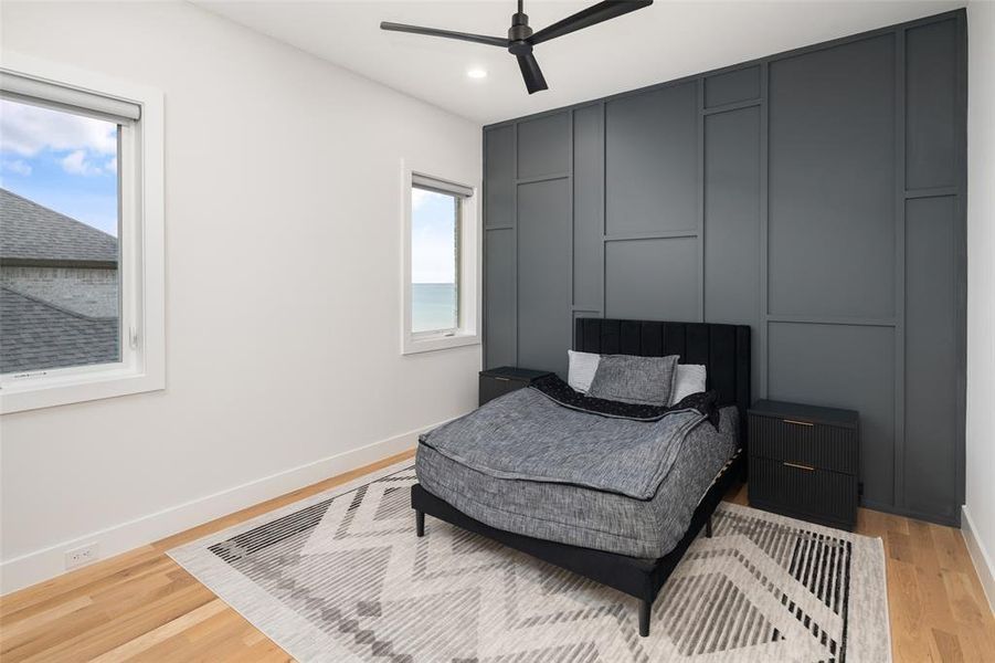Second-floor secondary bedroom featuring hardwood floors, a striking accent wall, and beautiful lake views that bring natural light and scenery into the space. Complete with a private ensuite bath and oversized walk-in closet, offering both comfort and functionality.