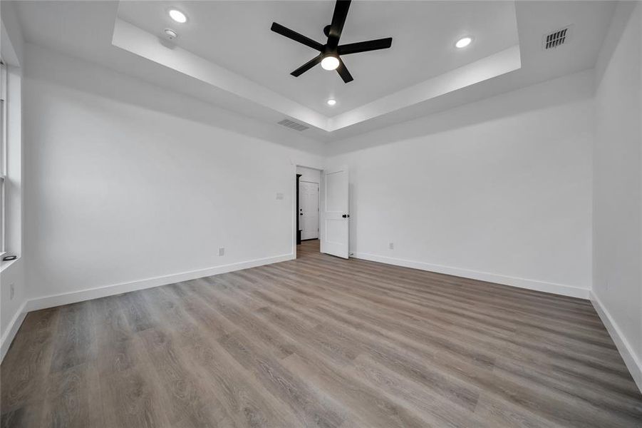 Spare room with a tray ceiling, ceiling fan, and light wood-type flooring