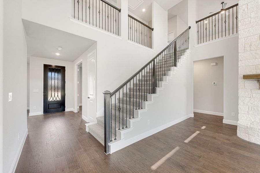 Two-story foyer with hardwood floors, iron staircase railing, and decorative front door with glass panels Two-story foyer with hardwood floors, iron staircase railing, and decorative front door with glass panels