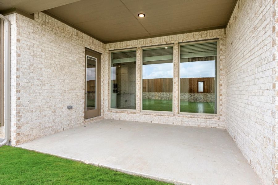Covered back patio with concrete floor, brick walls, large windows, and a glass door leading inside Covered back patio with concrete floor, brick walls, large windows, and a glass door leading inside