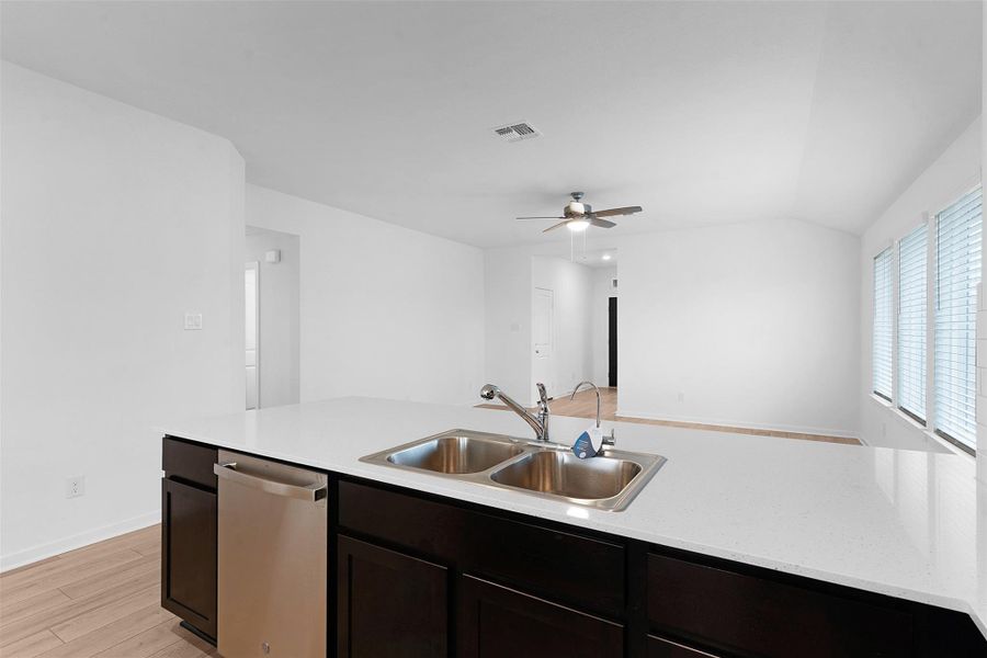 Kitchen featuring dishwasher, light wood-style floors, dark brown cabinets, light stone counters, and a ceiling fan
