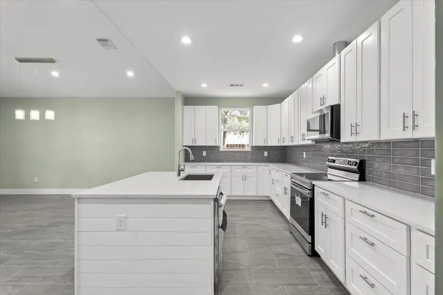 Kitchen featuring appliances with stainless steel finishes, light stone countertops, tasteful backsplash, a kitchen island with sink, and white cabinetry