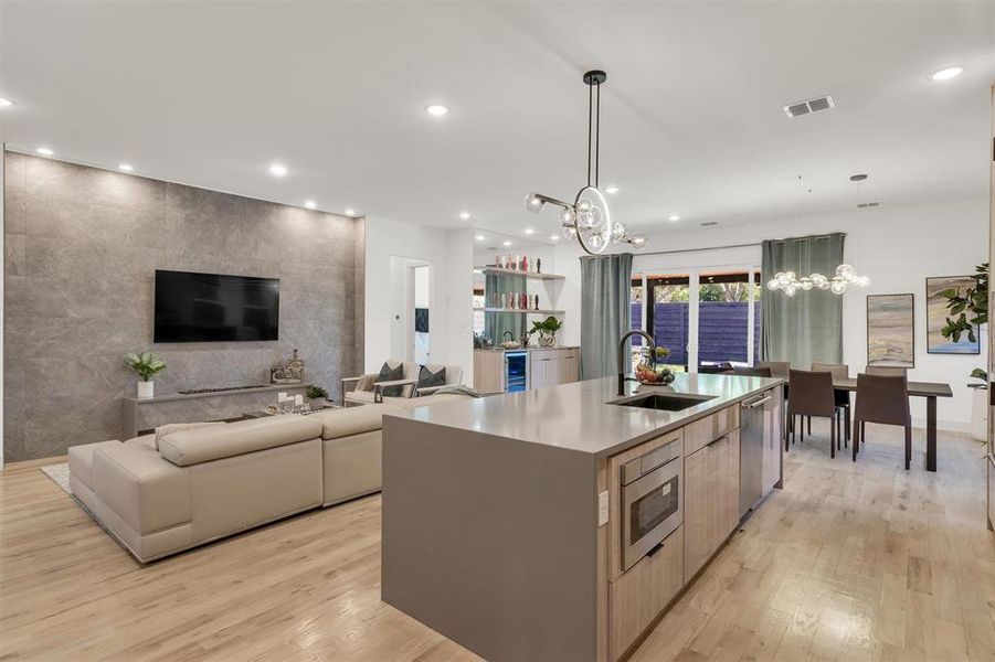 Kitchen with light hardwood / wood-style floors, appliances with stainless steel finishes, a large island with sink, pendant lighting, and sink