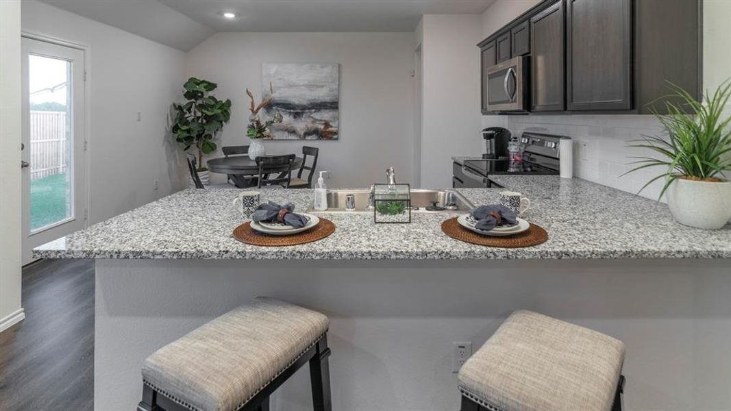 Kitchen with a peninsula, tasteful backsplash, a breakfast bar area, stainless steel appliances, and dark wood finished floors