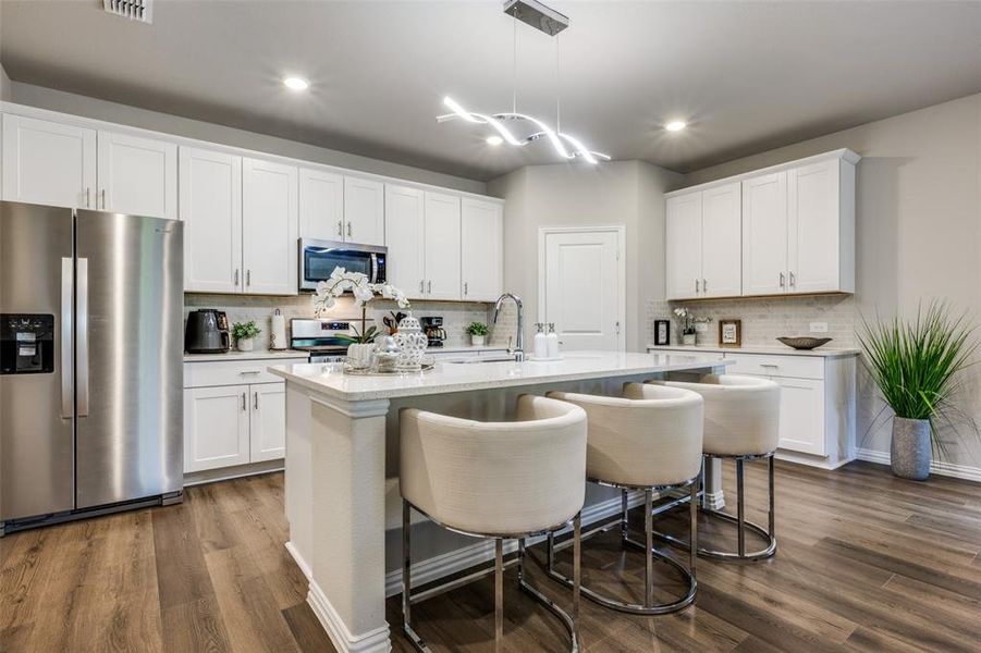 Kitchen with appliances with stainless steel finishes, a breakfast bar area, white cabinetry, hanging light fixtures, and dark wood-style flooring Kitchen with appliances with stainless steel finishes, a breakfast bar area, white cabinetry, hanging light fixtures, and dark wood-style flooring