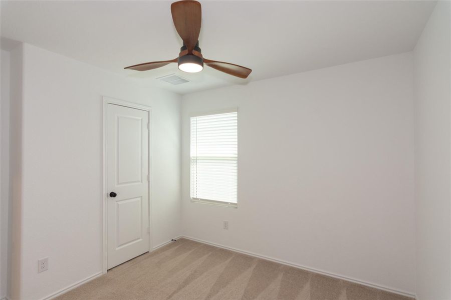 Carpeted room featuring a ceiling fan with integrated lighting, a paneled interior door with matte black hardware, and a window with horizontal blinds