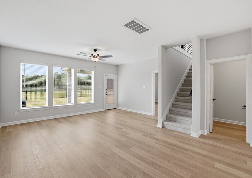 Living room featuring large windows, wood-look flooring, and a staircase view.
